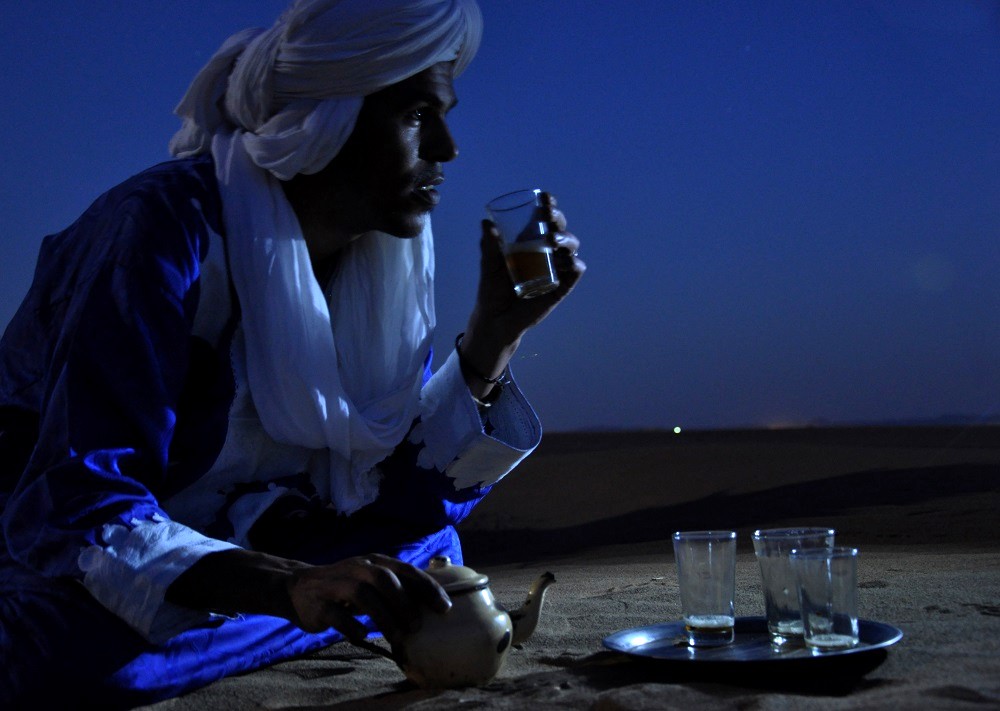 Hombre tomando té en el desierto de Marruecos al anochecer